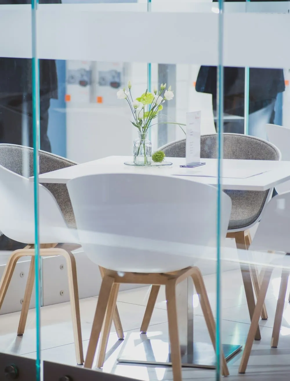 A meeting room seen through a glass wall, white chairs drawn up to a long table.